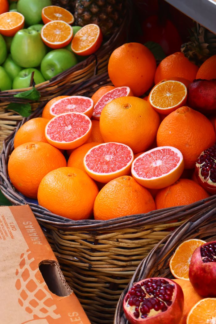 Colorful arrangement of citrus fruits and pomegranates in wicker baskets at a market.